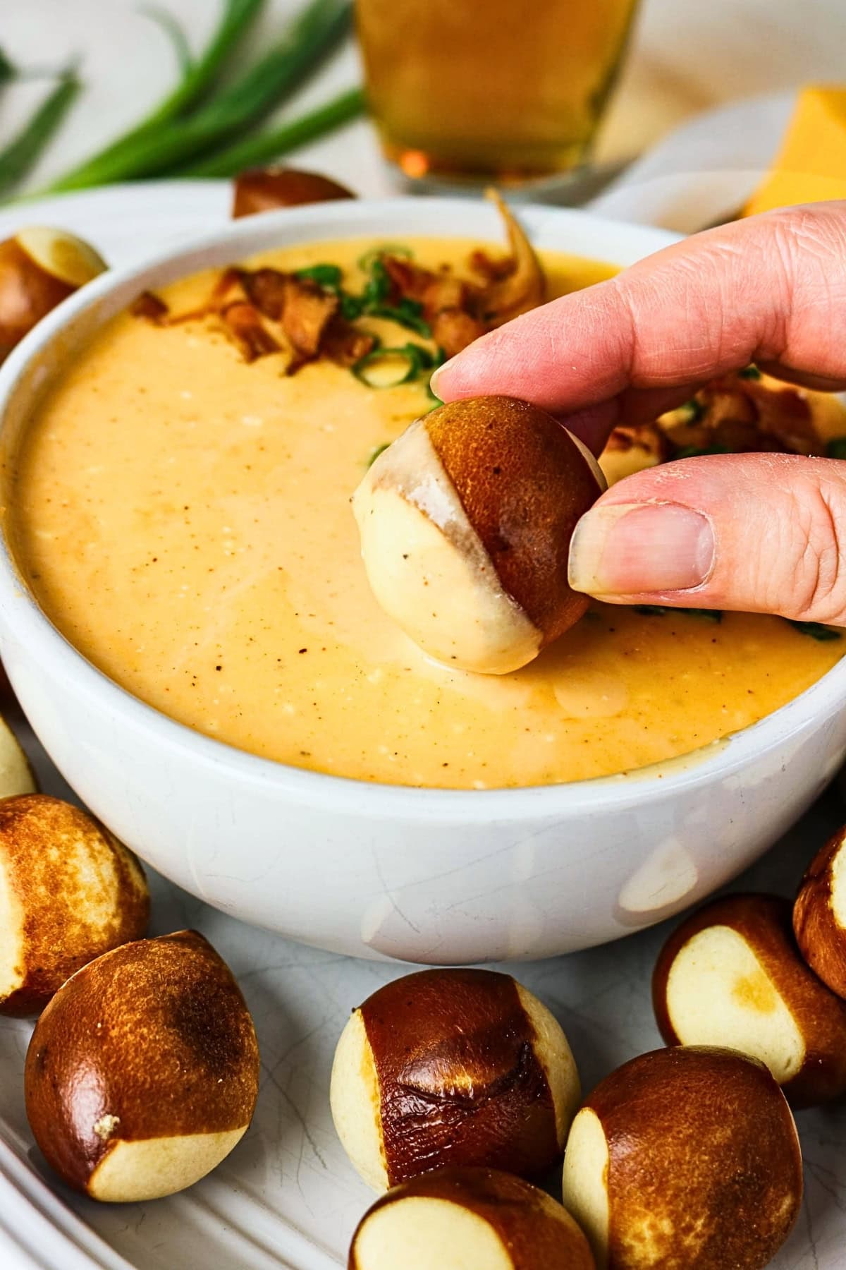 Hand dipping a pretzel bite into creamy cheese dip in a white bowl.