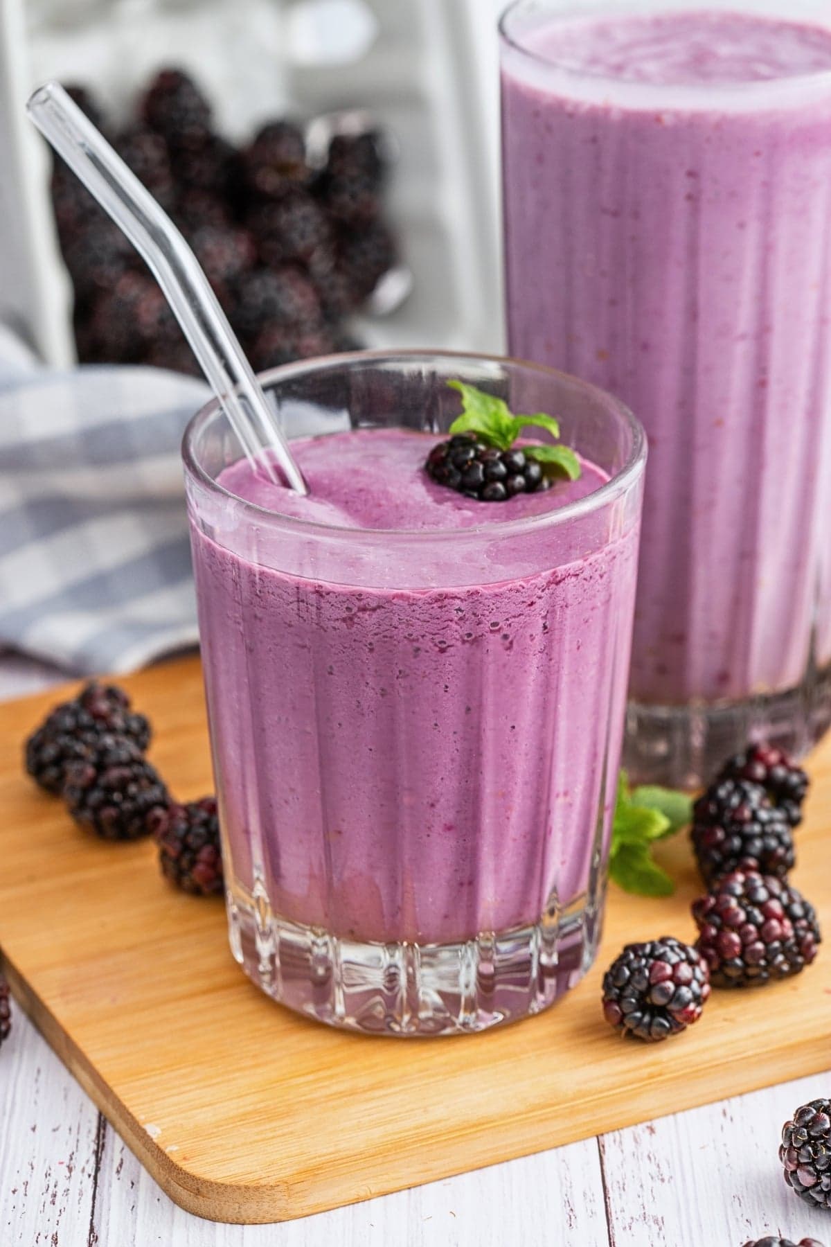 A glass of blackberry smoothie with a straw, garnished with a blackberry and mint.