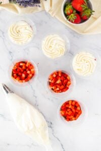 Six cups with whipped cream and diced strawberries, plus a piping bag nearby.