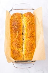 Two loaves of cheesy herb bread in a parchment-lined glass baking dish.