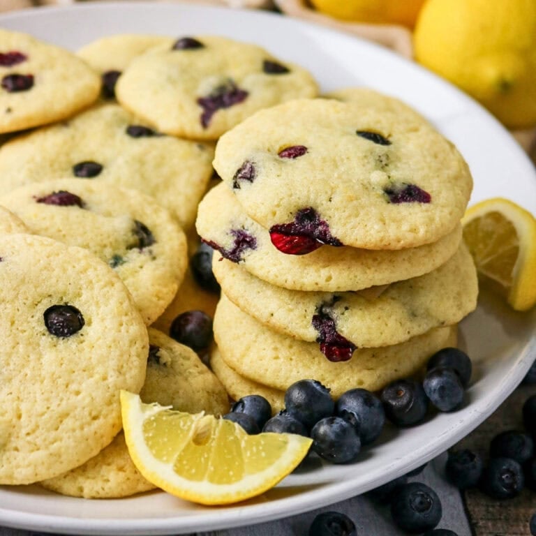 A plate of blueberry cookies with fresh blueberries and lemon slices.