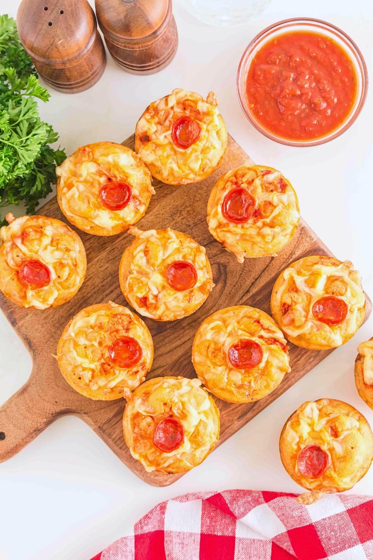Mini pepperoni pizza muffins on a wooden board with marinara sauce and parsley.