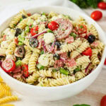 A bowl of rotini pasta salad with cherry tomatoes, olives, cheese, and salami.