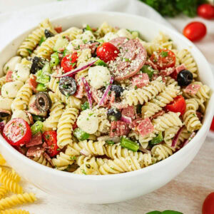 A bowl of rotini pasta salad with cherry tomatoes, olives, cheese, and salami.