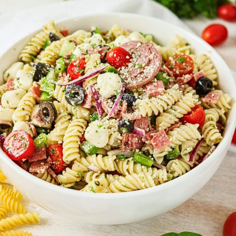 A bowl of rotini pasta salad with cherry tomatoes, olives, cheese, and salami.