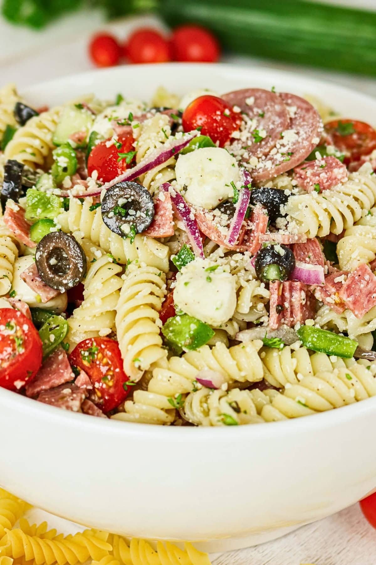 A bowl of Italian pasta salad with rotini, olives, tomatoes, cheese, and salami.