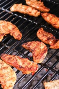 Seasoned chicken pieces grilling on a barbecue over hot coals.