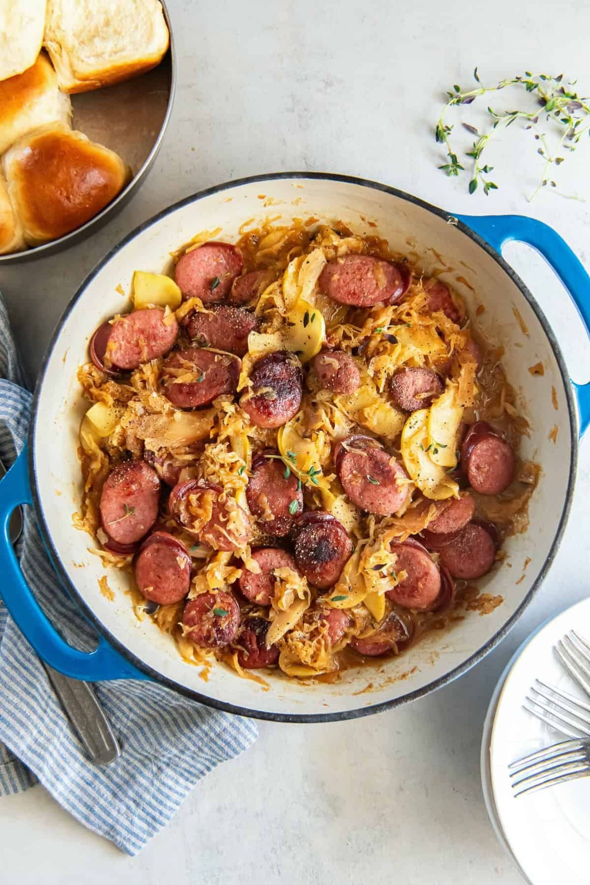 Kielbasa sausage meals with cabbage in a blue pot, served with rolls and plates.