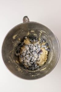 Metal mixing bowl with cookie dough and fresh blueberries on a white surface.