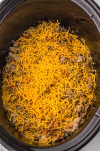 Shredded cheddar cheese topping a beef mixture in a slow cooker.