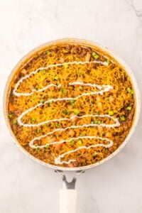 Pan of cooked ramen noodles topped with chopped veggies and a zigzag of white sauce.