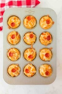 A muffin tin with twelve mini pizza muffins, each topped with a small pepperoni slice.