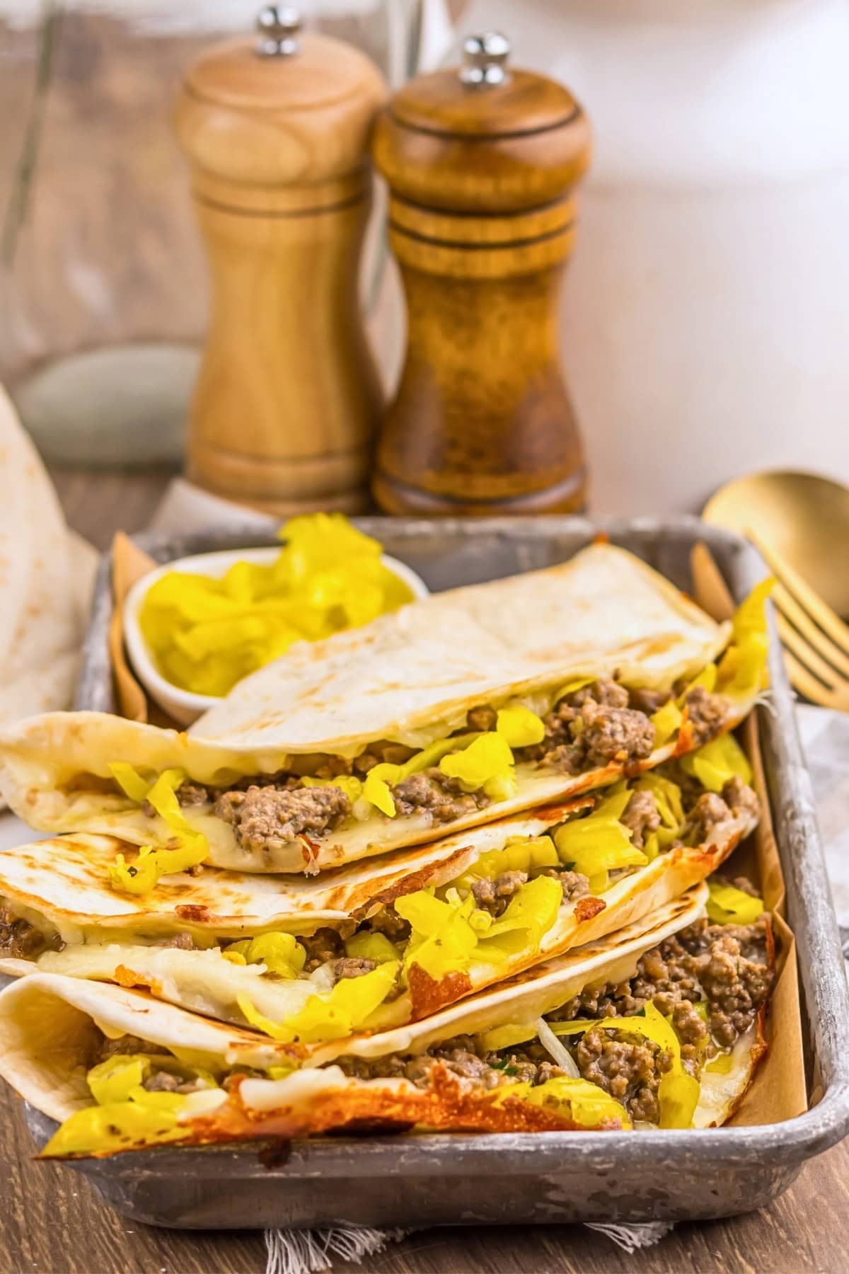 Tacos filled with ground beef and yellow peppers on a tray with condiments.