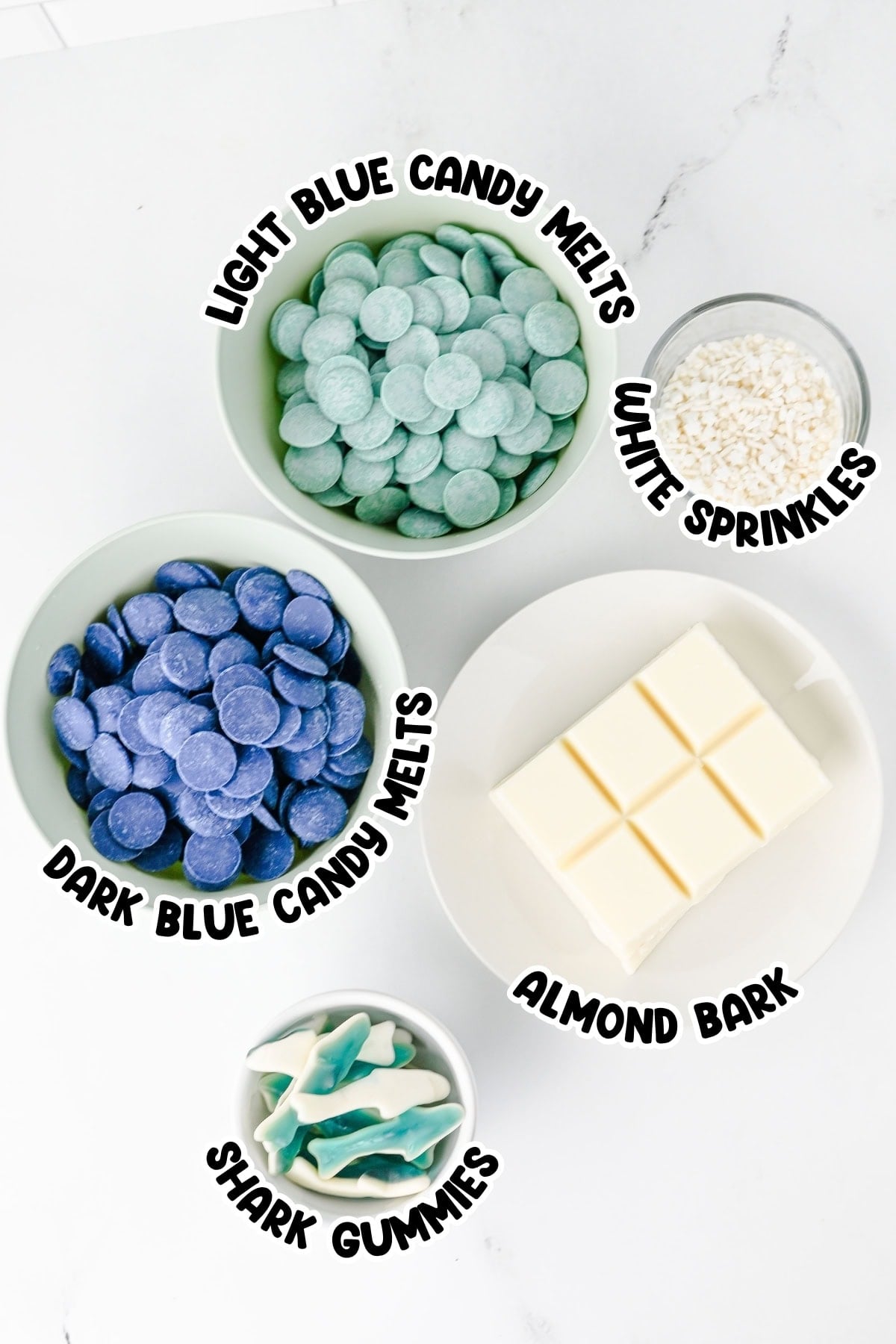 Bowls with candy melts, almond bark, white sprinkles, and shark gummies on a counter.