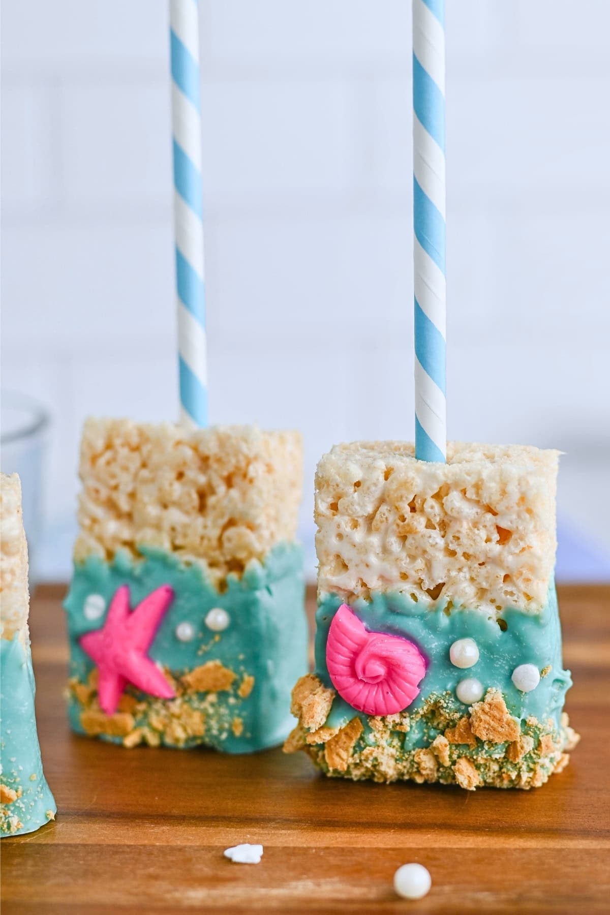 A rice crispy treat on a stick, half dipped in blue icing with seashell decorations.