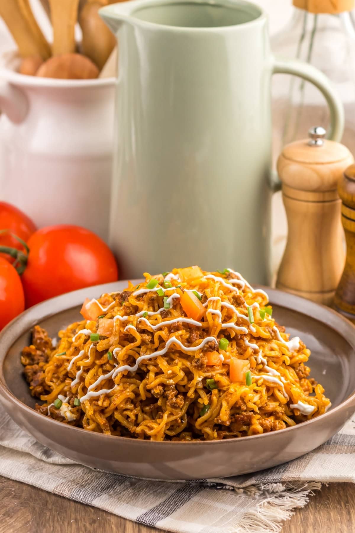 A plate of seasoned noodles topped with diced tomatoes and a creamy drizzle.