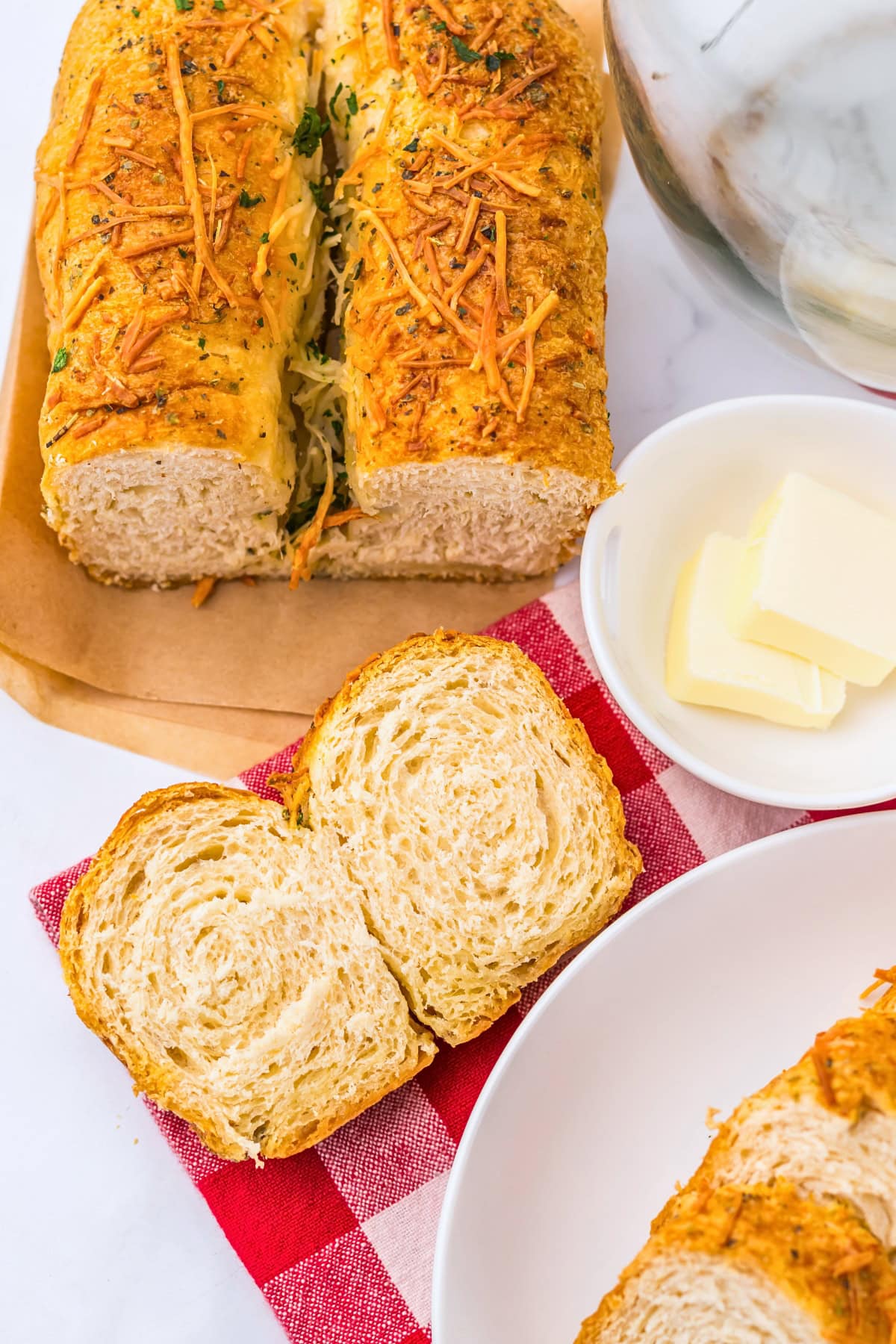 Sliced loaf of cheesy bread with butter on a red checkered napkin.