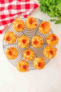 Mini pizza muffins with pepperoni on a cooling rack, next to a red checkered cloth.