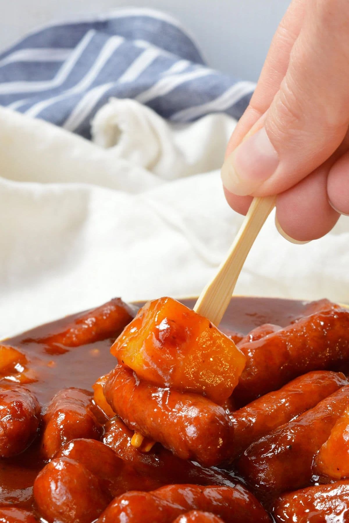 A hand uses a fork to pick up sausage and pineapple in tasty pineapple recipes.