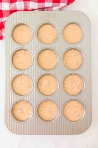 Muffin tin filled with batter, ready to be baked, on a white surface.