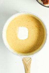 A saucepan of creamy cheese sauce with a dollop of sour cream on top.