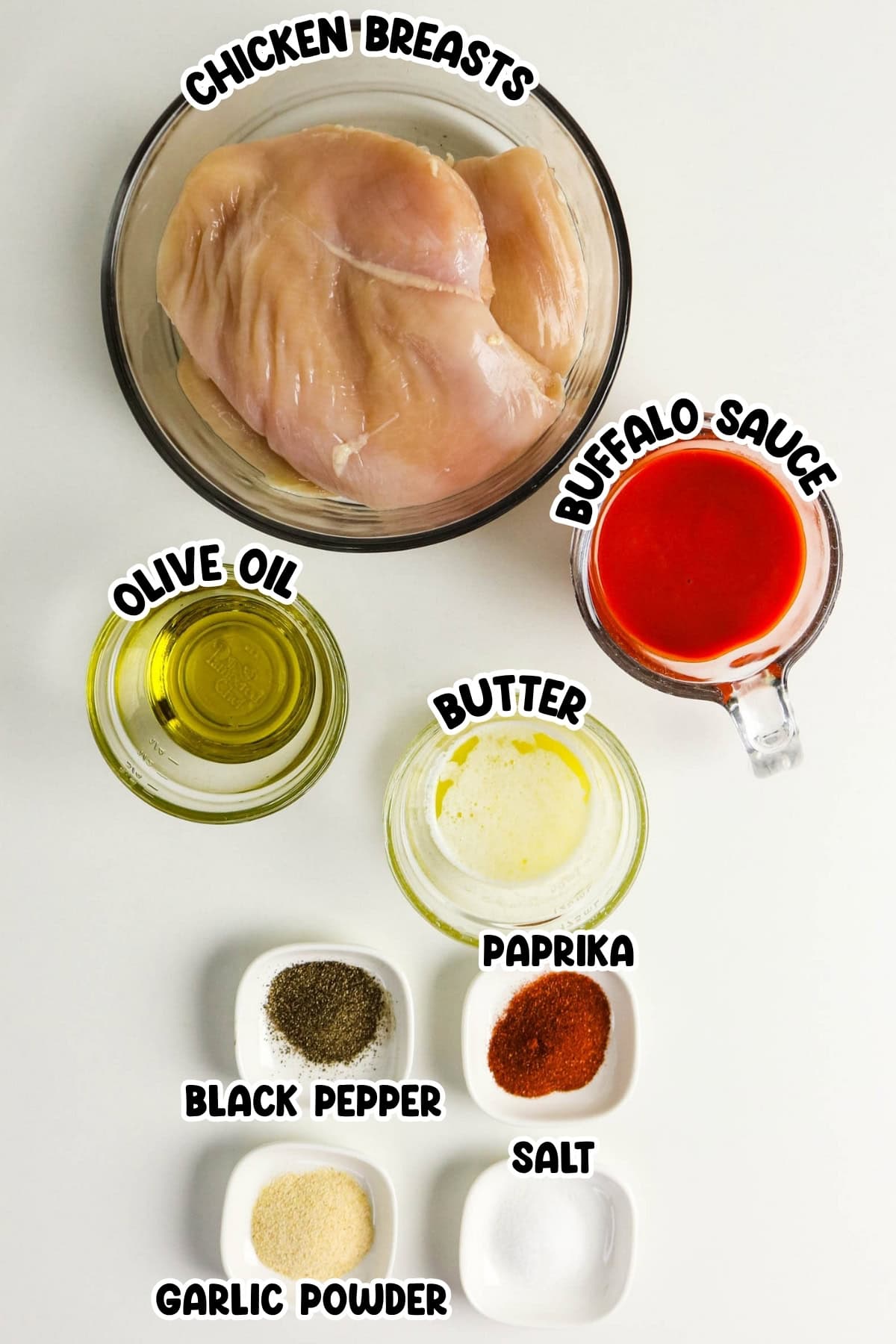 Raw chicken breasts, buffalo sauce, olive oil, butter, and assorted spices in bowls.