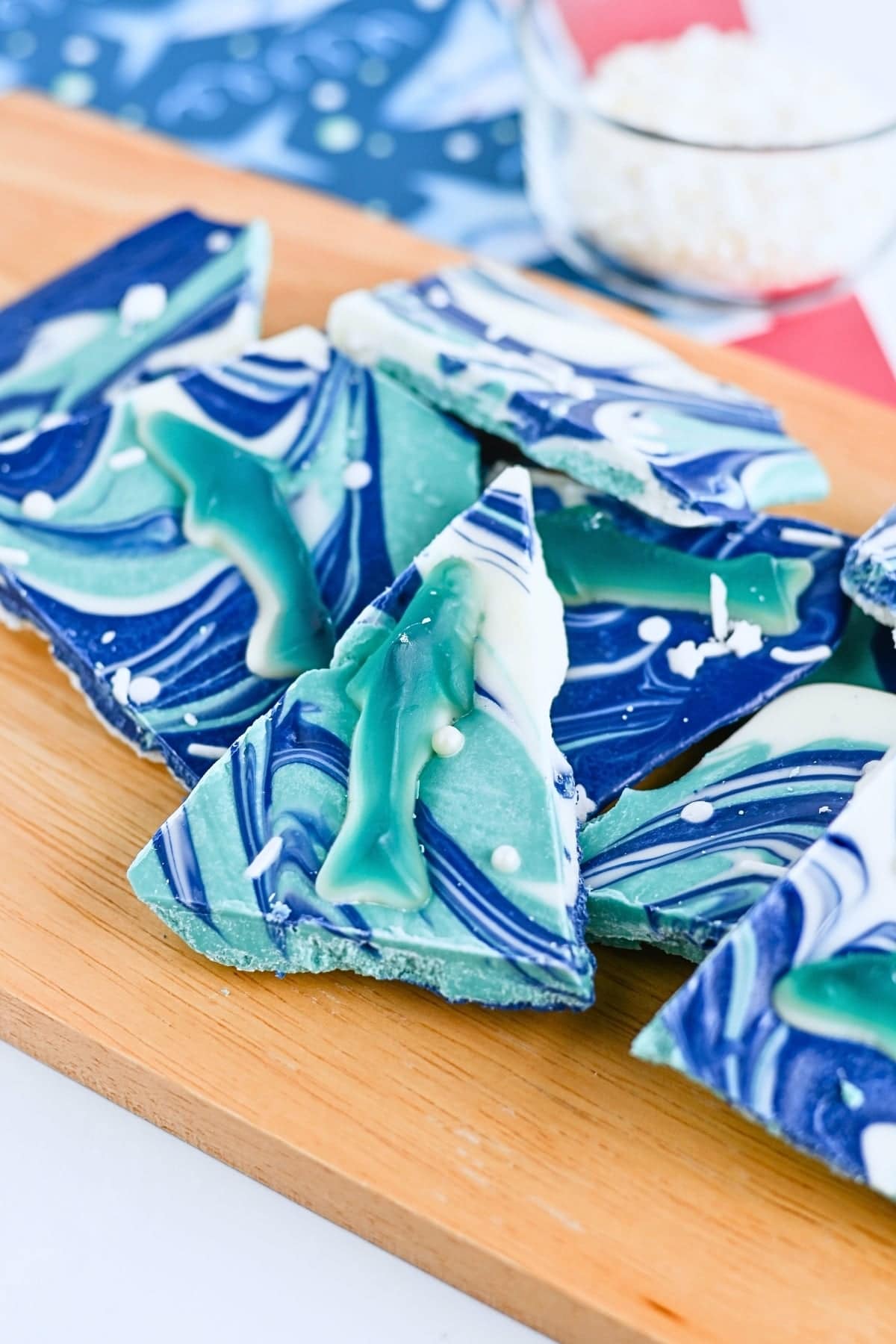 Blue and green marbled chocolate bark with white swirls on a wooden board.