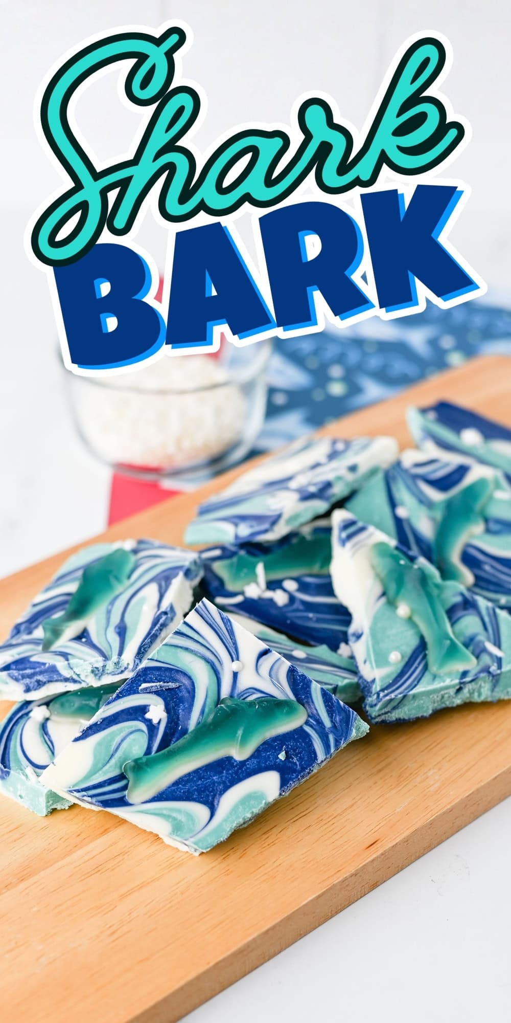 Blue and white swirled candy bark with shark shapes on a wooden board.