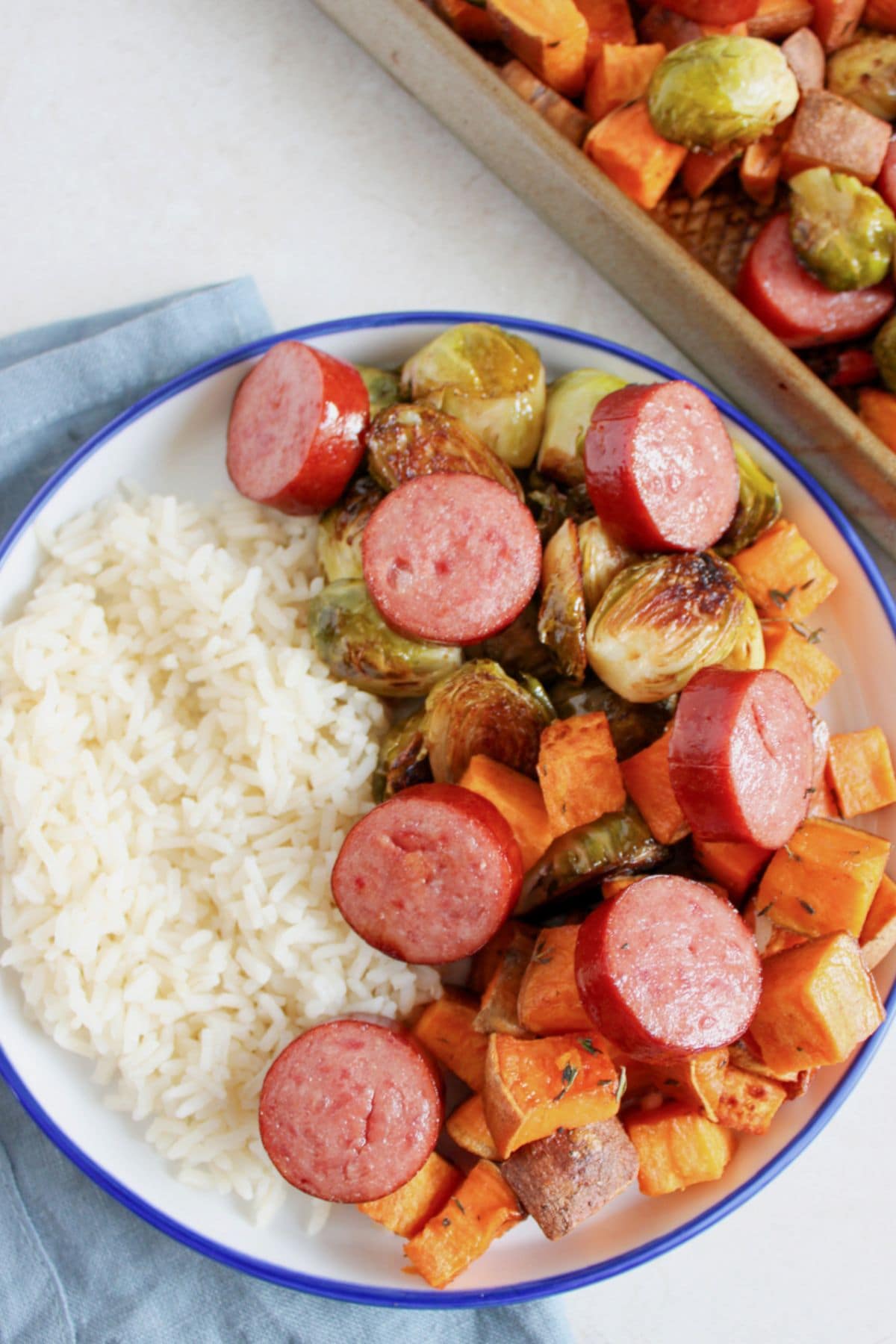A plate of white rice, kielbasa sausage meals, brussels sprouts, and sweet potatoes.