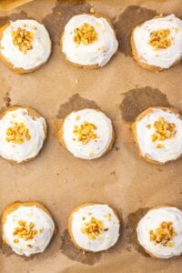 Nine frosted cookies topped with chopped nuts on parchment paper.