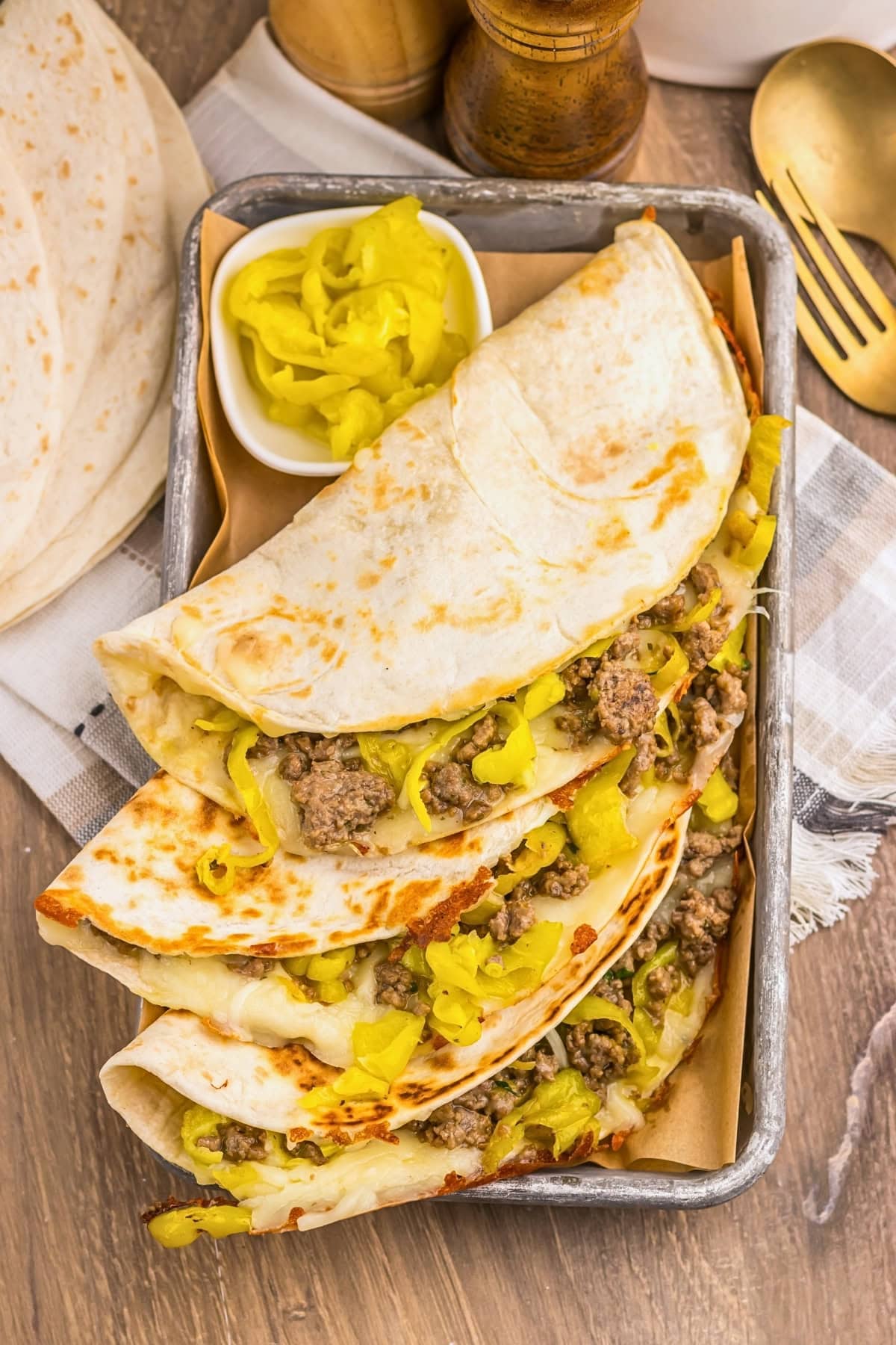Three beef and pepper tacos on a tray with a side of sliced yellow peppers.