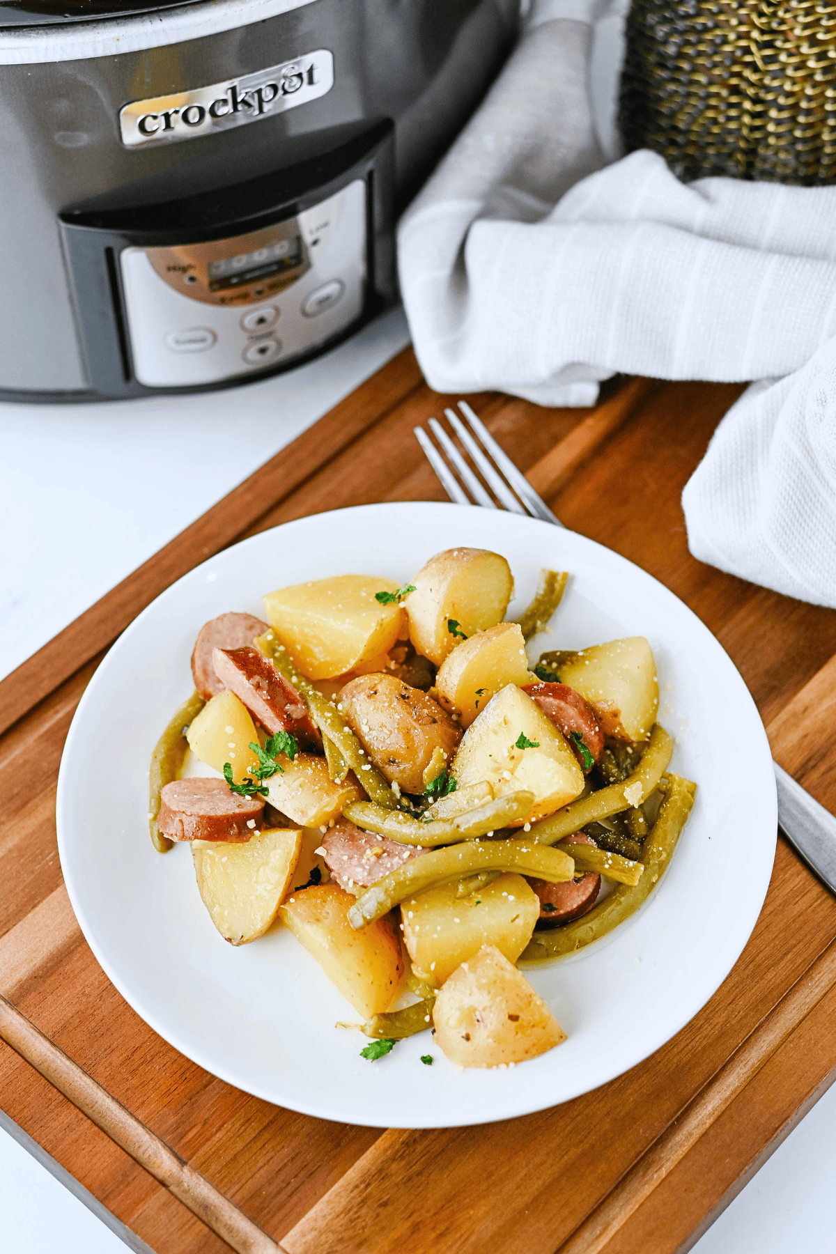 A plate of potatoes, green beans, and sausage sits beside a slow cooker.