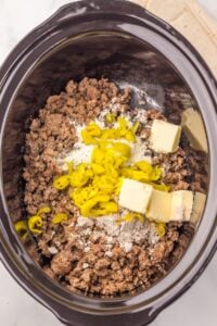 Ground beef, butter, sliced peppers, and seasonings in a slow cooker.
