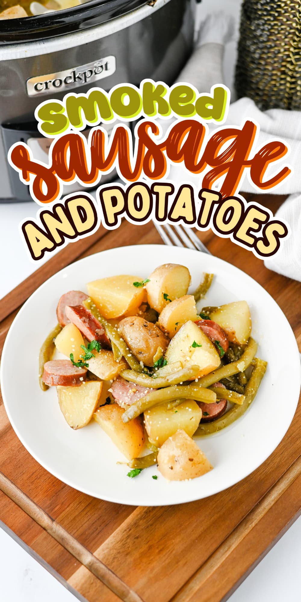 A plate of smoked sausage, potatoes, and green beans in front of a crockpot.
