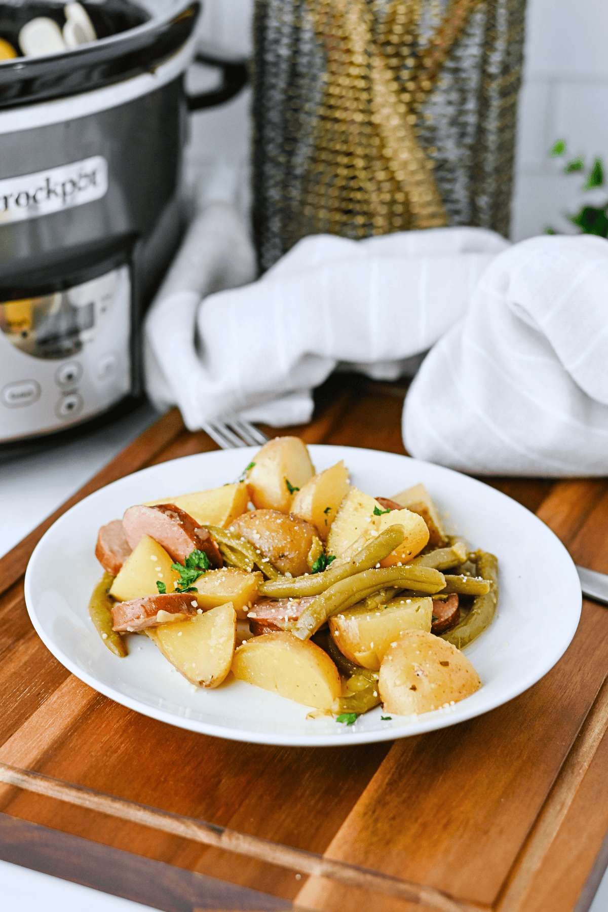 Sliced potatoes, sausage, and green beans served on a white plate.