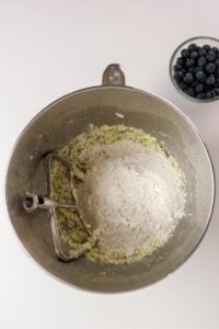 A mixing bowl with flour and batter beside a small bowl of blueberries.