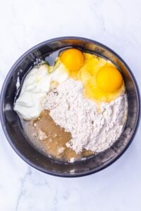 A bowl with two eggs, flour, yogurt, and liquid on a white surface.