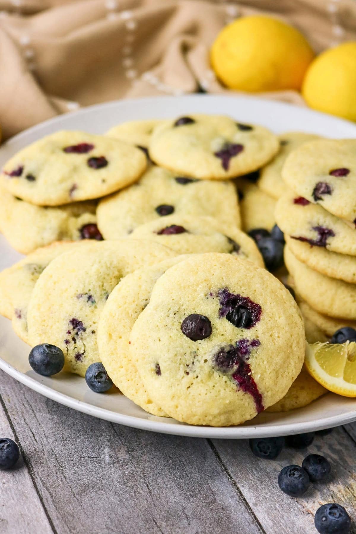A plate of blueberry cookies with fresh blueberries and lemons nearby.