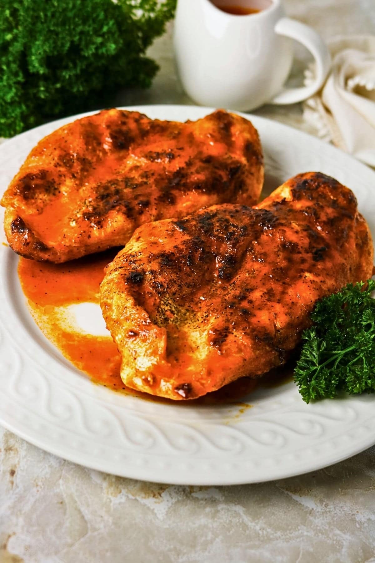 Two pieces of saucy, seasoned chicken breast on a white plate with parsley.
