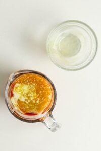 A glass measuring cup with sauce next to an empty glass bowl on a white surface.