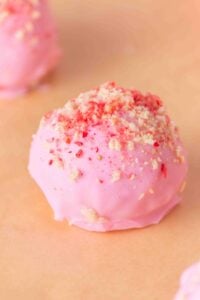 Pink truffle topped with crumbled crumbs on a peach-colored surface.