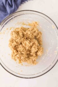 A glass bowl with cookie dough mixture and a blue cloth nearby.