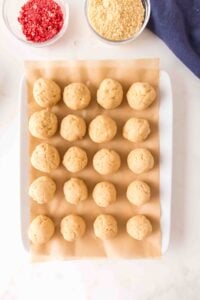 A tray of 20 unbaked dough balls on parchment paper, with toppings nearby.