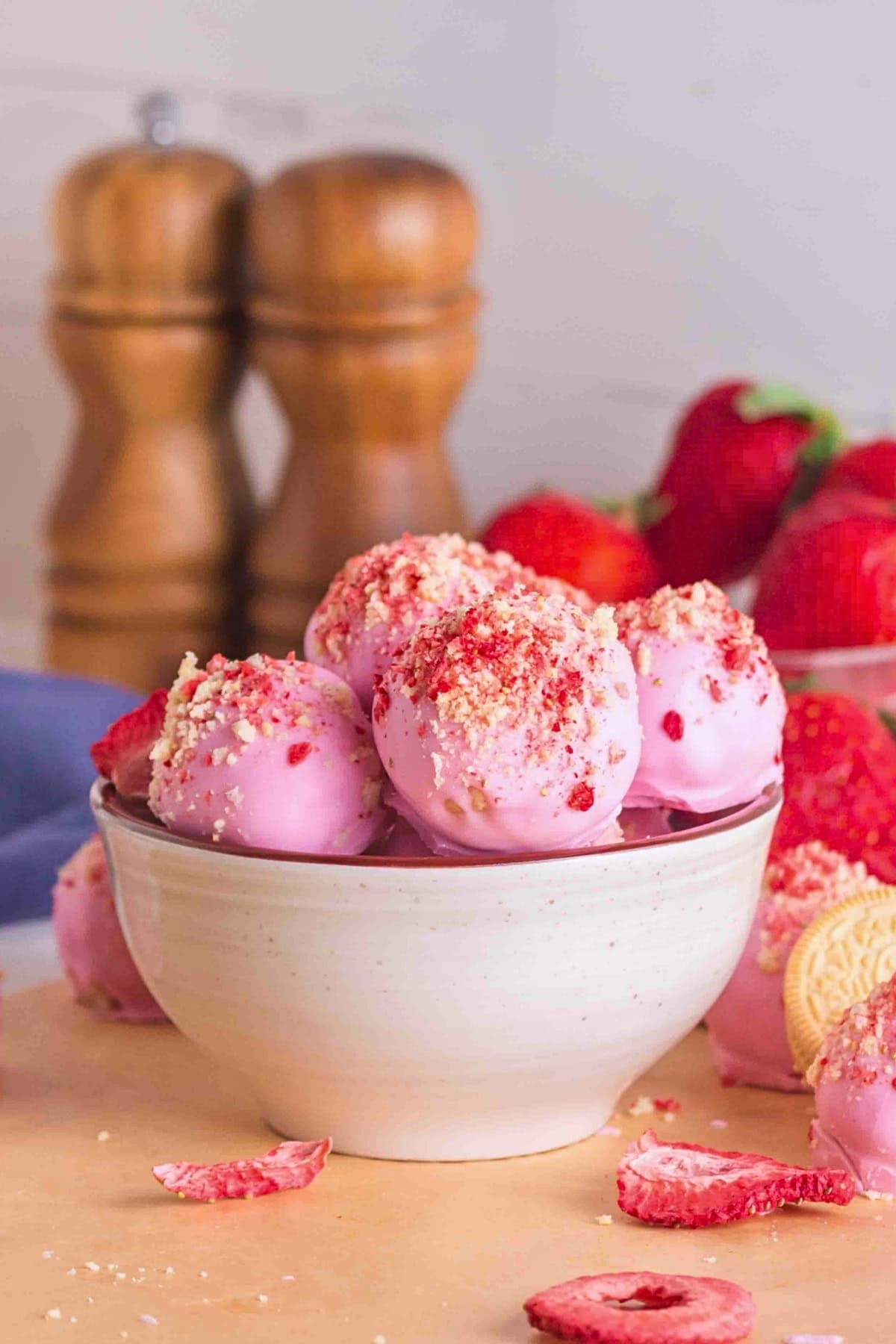 A bowl of pink strawberry truffles topped with crumbled cookies and strawberries.