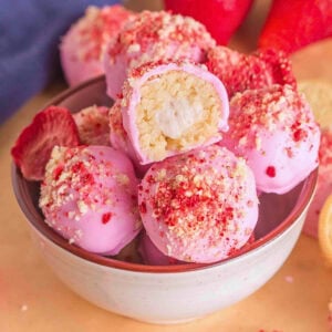 A bowl of pink, sprinkle-topped truffles, one with a creamy center exposed.