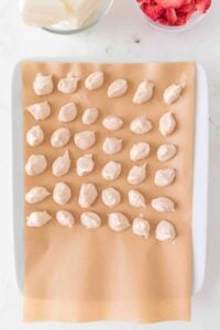 A tray with rows of small cream dollops on parchment paper.