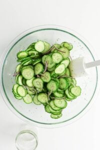Sliced cucumber and red onion salad in a glass bowl with a white spatula.
