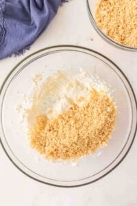 Glass bowl with creamy mixture and crushed crumbs, next to another bowl of crumbs.