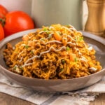 A plate of spicy noodles topped with diced tomatoes, sauce, and chopped herbs.
