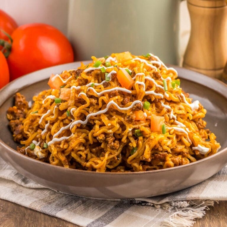 A plate of spicy noodles topped with diced tomatoes, sauce, and chopped herbs.